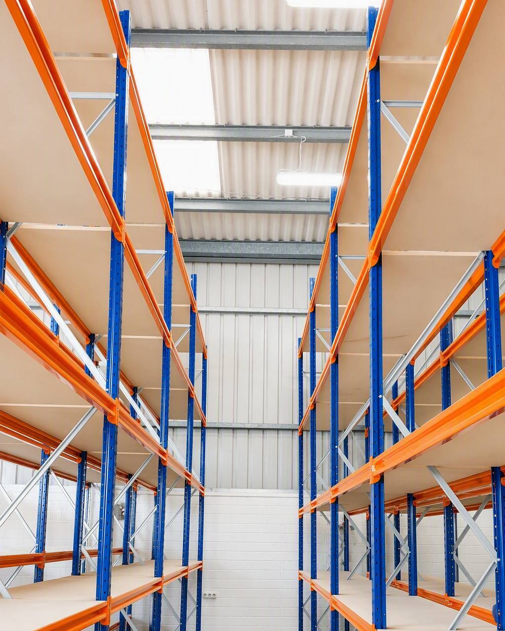 Tall pallet racking run with orange beams and blue uprights seen down the aisle