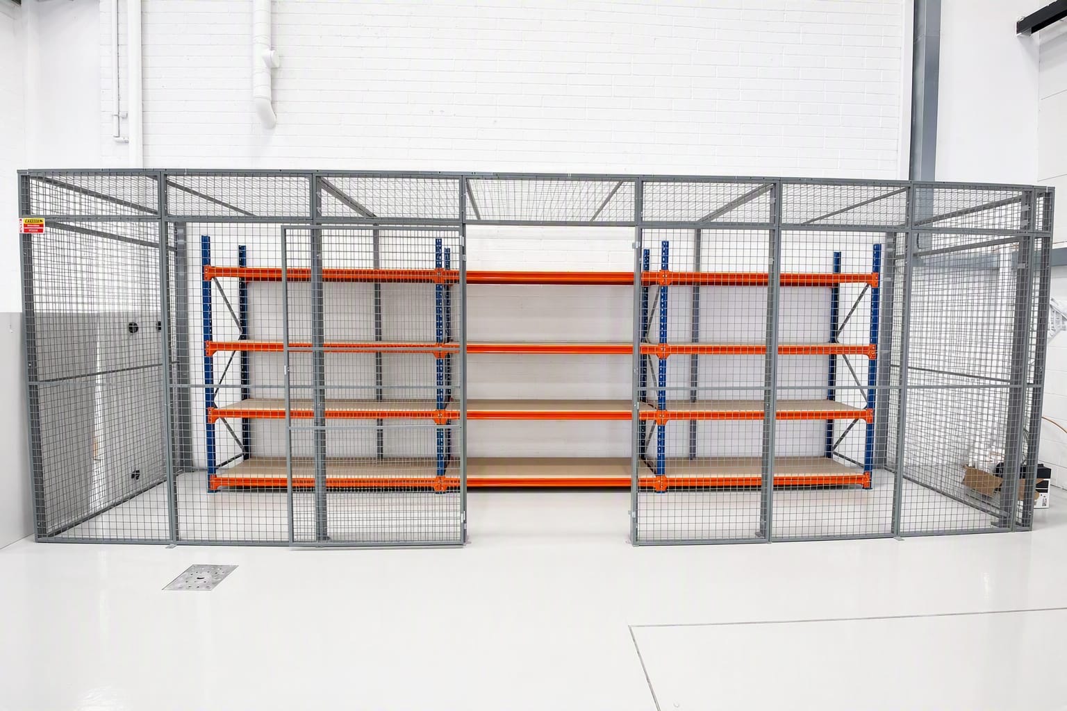 Grey steel mesh security cage with a mesh roof and two open gates, around a run of orange and blue shelving